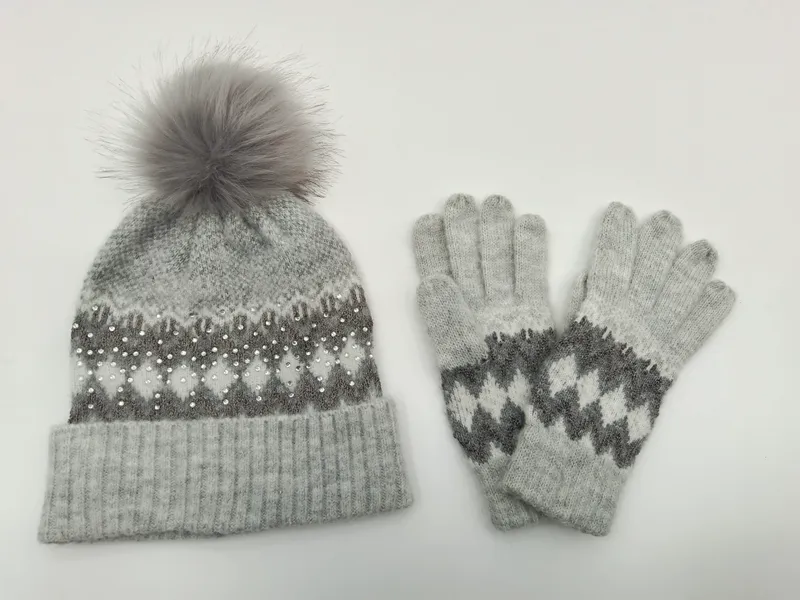 Graue Fair-Isle-Strickmütze mit Kunstfell-Bommel und Perlenapplikationen neben passenden Strickhandschuhen als Set