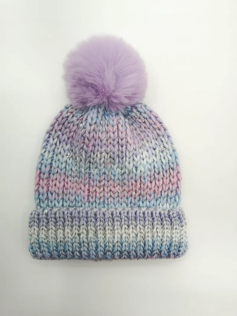 Grob gestrickte Beanie in Pastell-Ombre aus Lila, Blau und Rosa mit silbernen Pailletten und lavendelfarbenem Kunstfell-Bommel auf weißem Hintergrund