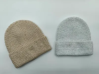 Zwei grob gestrickte Beanies nebeneinander: eine beige ohne Krempe und eine hellgraue mit umgeschlagenem Rand, auf weißem Hintergrund