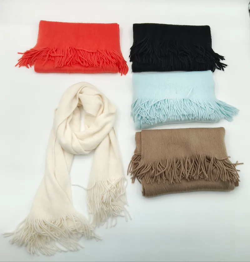 Fünf weiche Fransenschals in Creme, Schwarz, Rot, Hellblau und Beige auf weißem Hintergrund, einer offen drapiert