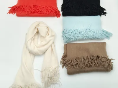 Fünf weiche Fransenschals in Creme, Schwarz, Rot, Hellblau und Beige auf weißem Hintergrund, einer offen drapiert