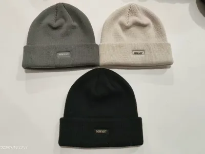 Drei Rippenstrickmützen mit gefaltetem Bund in Anthrazit, Cremeweiß und Schwarz auf weißer Oberfläche mit Logo-Patch