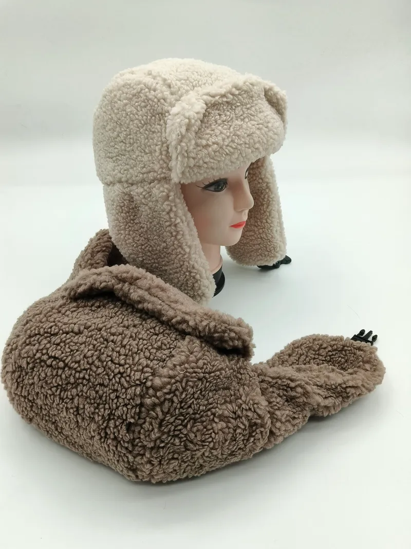 Zweifarbige Sherpa-Mütze in Creme und Beige mit weichem Fleece-Material und herunterklappbaren Ohrenschützern auf Hutständer