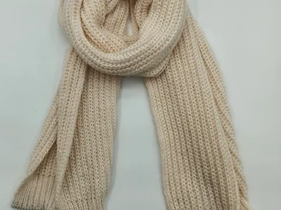Cremefarbener Strickschal mit strukturierter Waffeloptik, locker aufgerollt und flach drapiert, Detailaufnahme der Textur