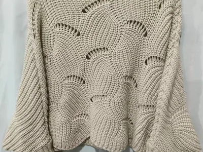 Cremefarbener weiter Häkel-Strickpullover mit dekorativem Fächerstich und ausgestellten Ärmeln auf einem Kleiderbügel