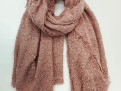 Großformatiger Strickschal in gedämpftem Rosaton mit glitzernden Pailletten und fransigem Saum, locker aufgerollt auf weißem Hintergrund