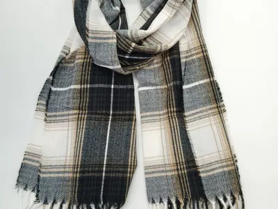 Gefalteter Tartan-Schal in den Farben Schwarz, Weiß und Sandbeige mit gedrehten Fransenenden auf weißem Untergrund