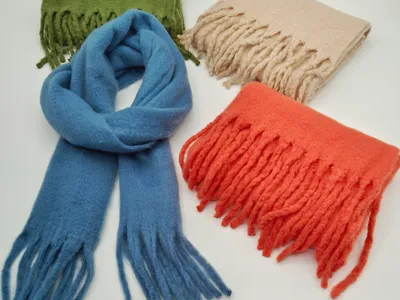 Vier Wollmix-Schals mit Fransen in Blau, Olivgrün, Beige und Korallorange, nebeneinander auf weißem Hintergrund präsentiert