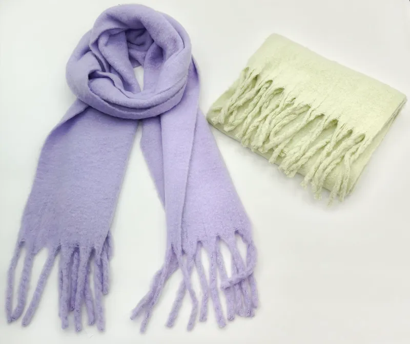 Zwei weiche Flauschschals mit Fransenenden: einer in Lavendel offen geloopt, einer in Mintgrün gefaltet, auf weißem Hintergrund