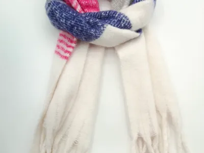 Aufgerollter XXL-Winterschal mit Karomuster in Pink, Blau und Creme sowie langen Fransenenden auf weißem Hintergrund