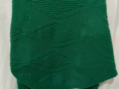 Rückansicht eines smaragdgrünen Strick-Ponchos mit erhabenem Rautenmuster auf einem Kleiderbügel