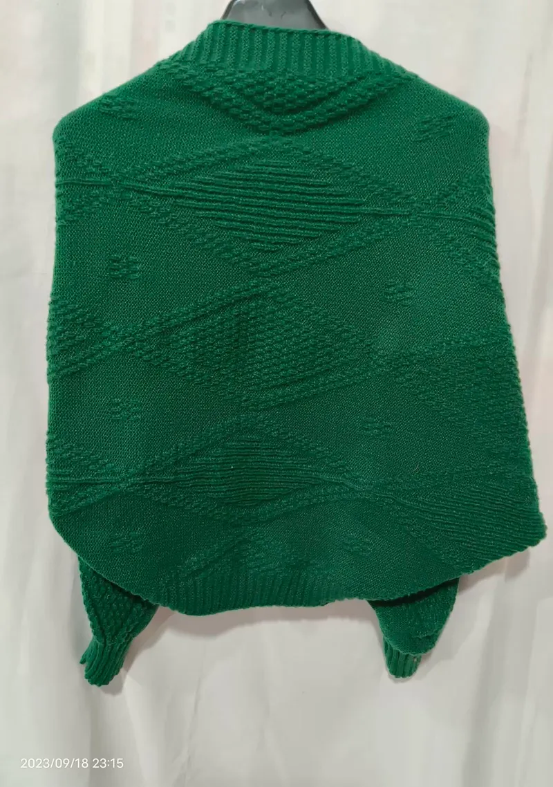 Rückansicht eines smaragdgrünen Strick-Ponchos mit erhabenem Rautenmuster auf einem Kleiderbügel
