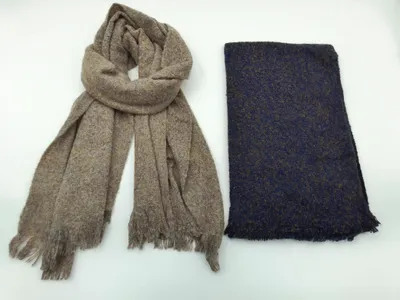 Zwei gewebte Schals mit Fransenrand nebeneinander: ein drapierter Taupe-Melange-Schal und ein gefalteter Marineblau-Tweedschal auf weißem Hintergrund