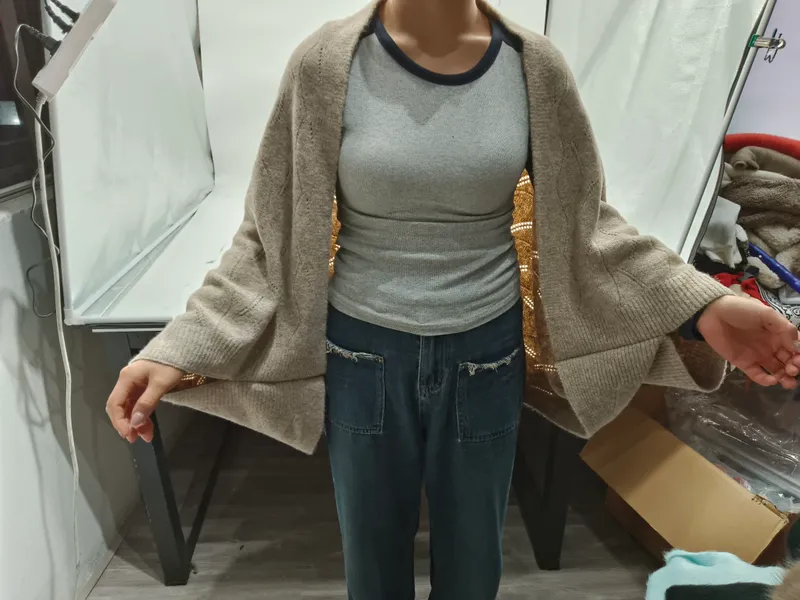 Frau trägt einen übergroßen beigen Strick-Cardigan mit offenem Vorderteil über einem grauen Rippentop mit blauen Jeans