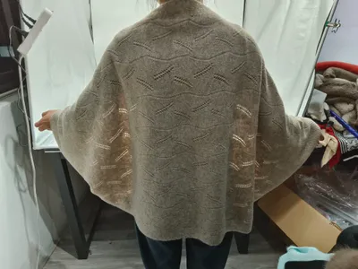 Rückenansicht einer Frau in einem übergroßen beigen Pointelle-Strick Cardigan mit Fledermausärmeln und Wellenmuster-Spitzenstrick