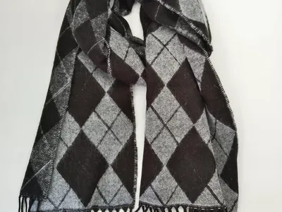 Gestrickter Winterschal in Schwarz und Grau mit klassischem Rautenmuster und langen schwarzen Fransen, flach auf weißem Untergrund