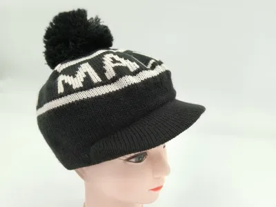 Gestrickte schwarze Wintermütze mit Schirm, auffälligem weißem Jacquard-Buchstabenprint und Bommel oben auf einer Hutform präsentiert