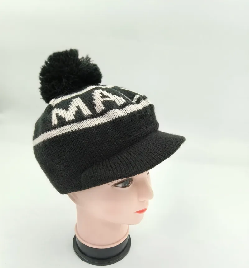Gestrickte schwarze Wintermütze mit Schirm, auffälligem weißem Jacquard-Buchstabenprint und Bommel oben auf einer Hutform präsentiert