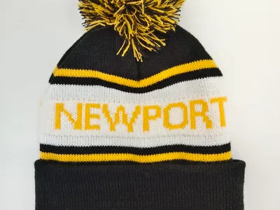 Gestreifte Strickmütze in Schwarz, Weiß und Gelb mit Newport-Schriftzug und großem zweifarbigem Bommel, freigestellt auf weißem Hintergrund