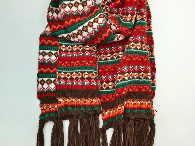 Aufgerollter Fair-Isle Strickschal in Rot, Grün, Orange und Weiß mit geometrischen Mustern und langen braunen Fransenden
