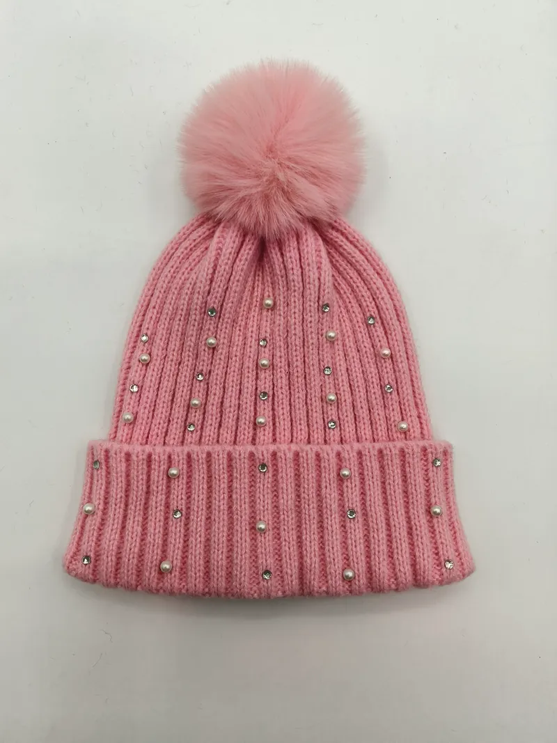 Rosa Rippenstrickmütze mit flauschigem Kunstfell-Bommel sowie Perlen- und Kristall-Strassstein-Verzierungen auf weißem Hintergrund