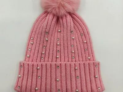 Rosa Rippenstrickmütze mit flauschigem Kunstfell-Bommel sowie Perlen- und Kristall-Strassstein-Verzierungen auf weißem Hintergrund