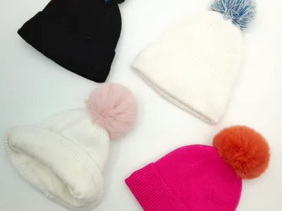 Vier Rippenstrickmützen mit bunten Bommeln in Schwarz, Weiß und Fuchsia-Pink, flach auf weißem Hintergrund angeordnet