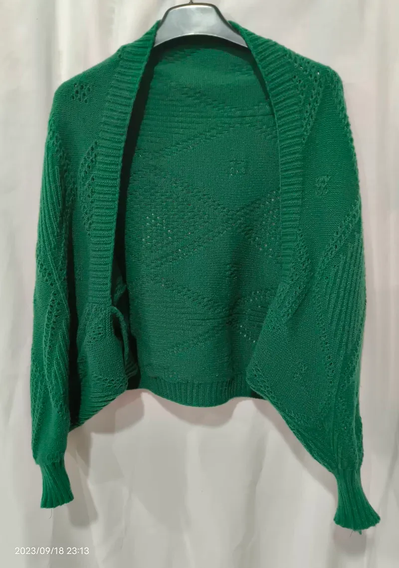 Offener smaragdgrüner Strickjacke mit Durchbruch-Rautenmuster und Rippenbündchen auf einem Kleiderbügel vor weißem Hintergrund