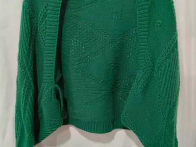 Offener smaragdgrüner Strickjacke mit Durchbruch-Rautenmuster und Rippenbündchen auf einem Kleiderbügel vor weißem Hintergrund