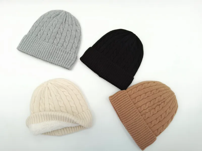 Vier Zopfmuster-Wintermützen in Grau, Schwarz, Creme und Beige flach auf weißem Hintergrund präsentiert