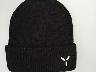 Schwarze Rippenstrickmütze mit Umschlagbündchen und kleinem weißem gestickten Y-Logo auf hellgrauem Hintergrund