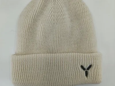 Cremefarbene Rippenstrickmütze mit breitem Umschlagbündchen und kleinem schwarzen gestickten Y-Logo, flach auf weißem Hintergrund