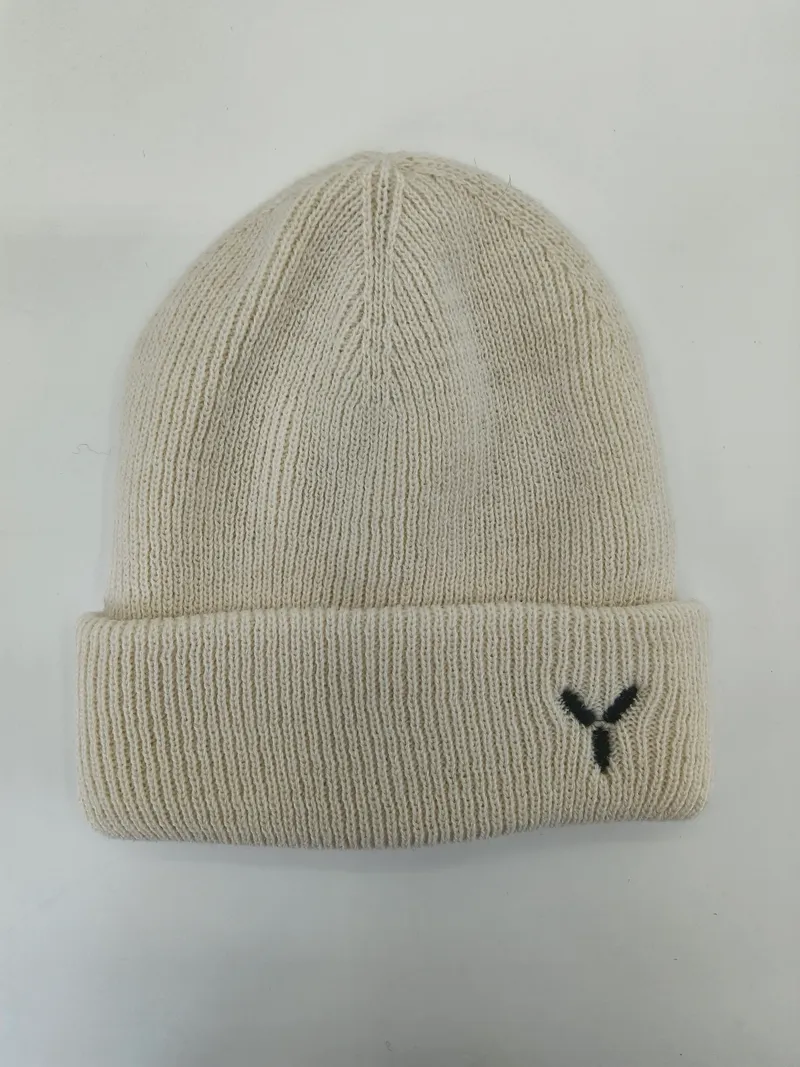 Cremefarbene Rippenstrickmütze mit breitem Umschlagbündchen und kleinem schwarzen gestickten Y-Logo, flach auf weißem Hintergrund