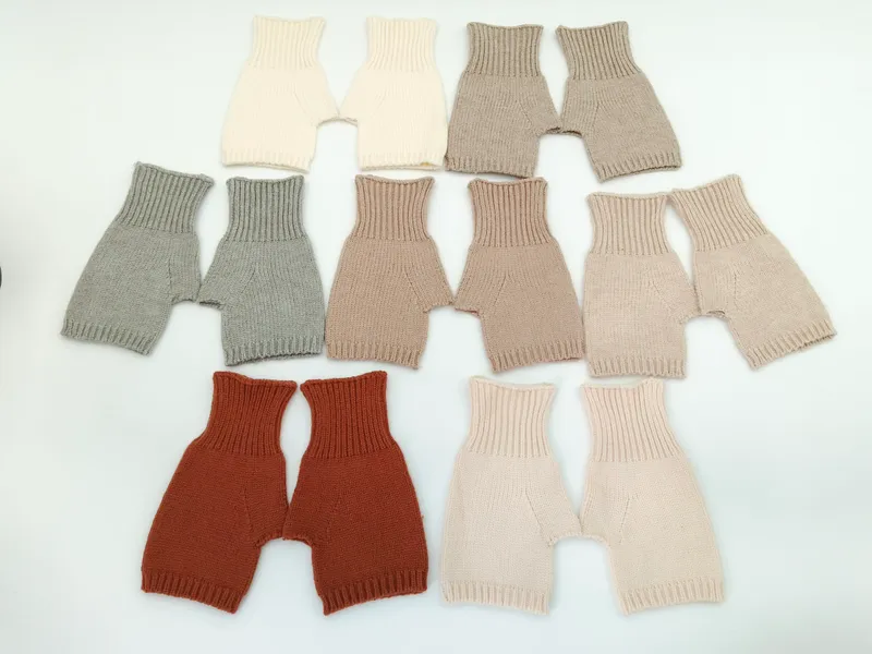 Sieben handgestrickte Baby-Shorts in den Farben Creme, Grau, Taupe, Beige, Rost, Rosa und Sand auf weißem Hintergrund