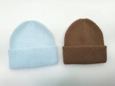 Zwei gerippte Strickmützen nebeneinander, eine in Babyblau, eine in Karamellbraun, jeweils mit umgeschlagenem Bund auf weißem Hintergrund