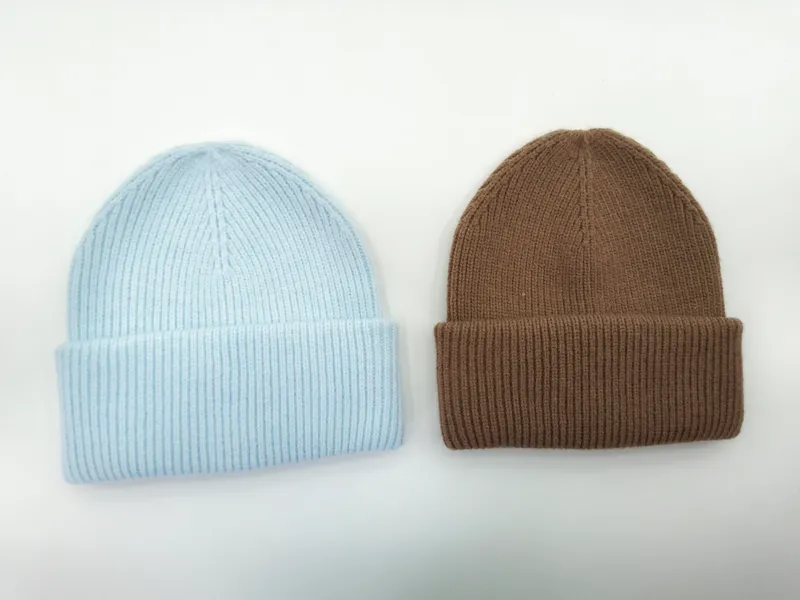 Zwei gerippte Strickmützen nebeneinander, eine in Babyblau, eine in Karamellbraun, jeweils mit umgeschlagenem Bund auf weißem Hintergrund