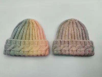 Zwei handgestrickte Beanies mit Zopfmuster-Bündchen, eine in Grün-Gelb-Pfirsich und eine in gedämpften Rosa-Taupe-Tönen