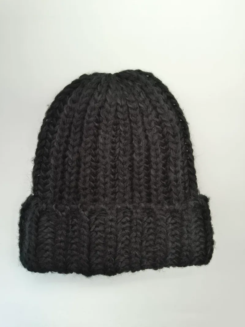 Schwarze grob gestrickte Beanie mit breitem Umschlagbund, handgemacht wirkend, flach auf weißem Hintergrund fotografiert
