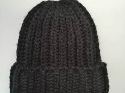 Schwarze grob gestrickte Beanie mit breitem Umschlagbund, handgemacht wirkend, flach auf weißem Hintergrund fotografiert