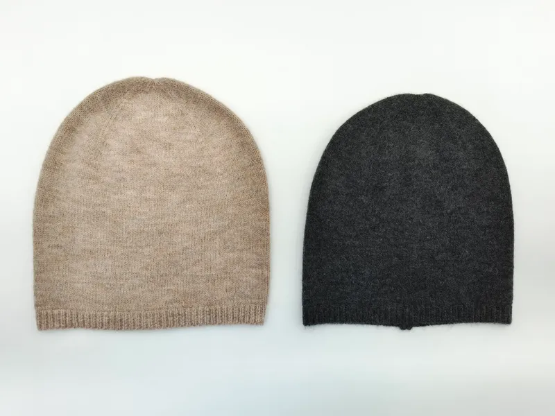 Zwei flach gelegte Kaschmir-Slouchy-Beanies nebeneinander in Oatmeal-Beige und Anthrazitgrau mit Rippenbund auf weißem Hintergrund