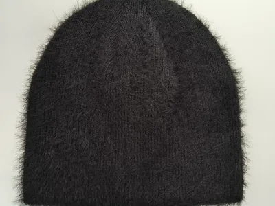 Schwarze Strickmütze mit flauschigen Mohair-artigen Fasern und gerippter Struktur, flach auf weißem Hintergrund liegend