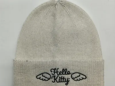 Creme-weiße Rippenstrick-Beanie mit Hello-Kitty-Engelflügel-Stickerei auf umgeschlagenem Mützenrand, flach fotografiert