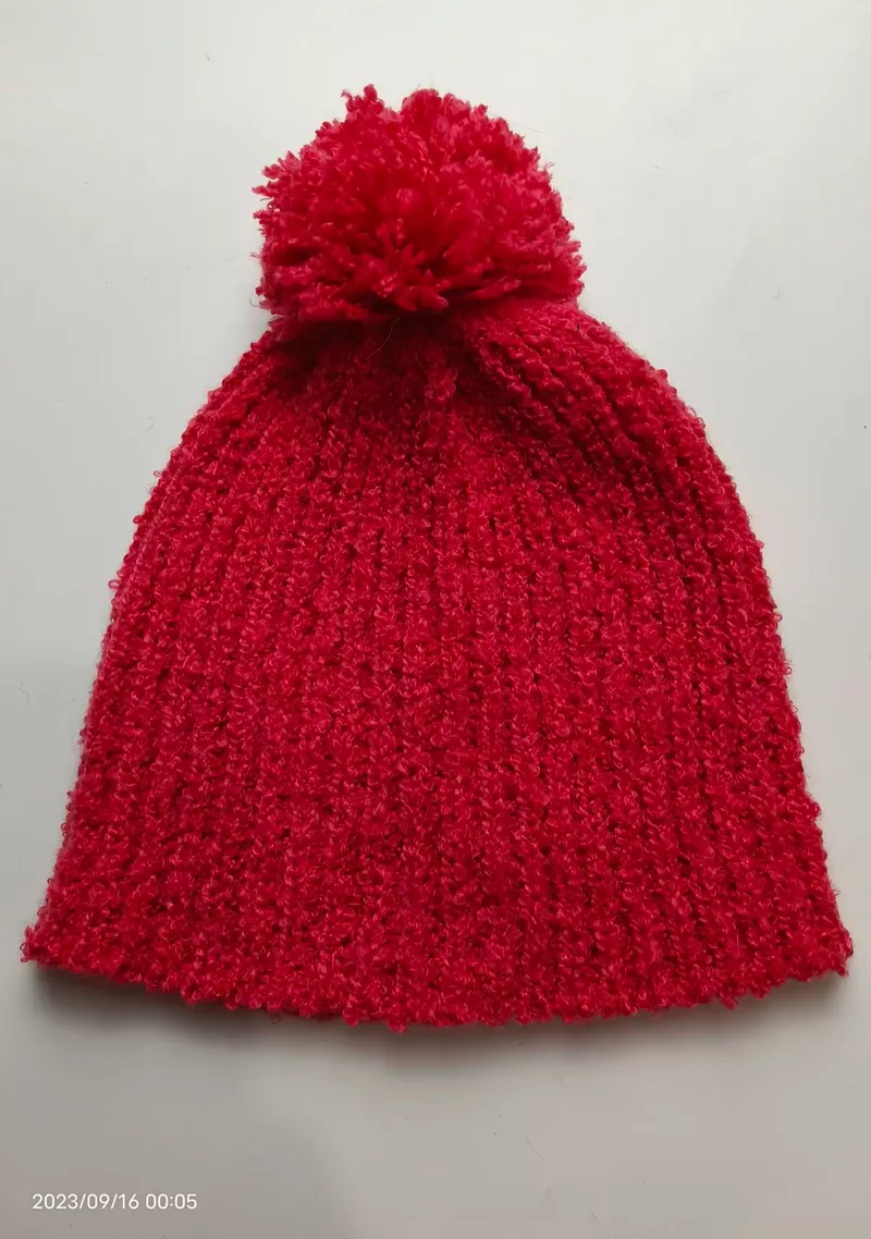 Rote strukturierte Rippenstrickmütze mit großem flauschigem Pompon auf der Spitze, flach auf weißem Hintergrund
