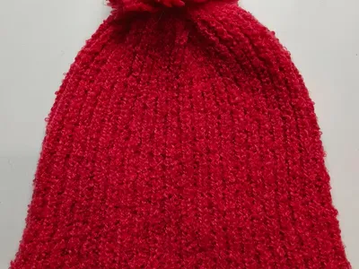 Rote strukturierte Rippenstrickmütze mit großem flauschigem Pompon auf der Spitze, flach auf weißem Hintergrund
