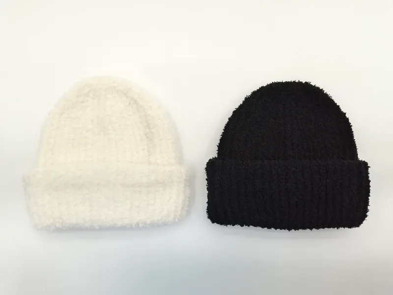 Zwei flauschige Rippenstrick-Beanies flach auf weißem Hintergrund, eine cremeweiß, eine schwarz, jeweils mit gefaltetem Bund