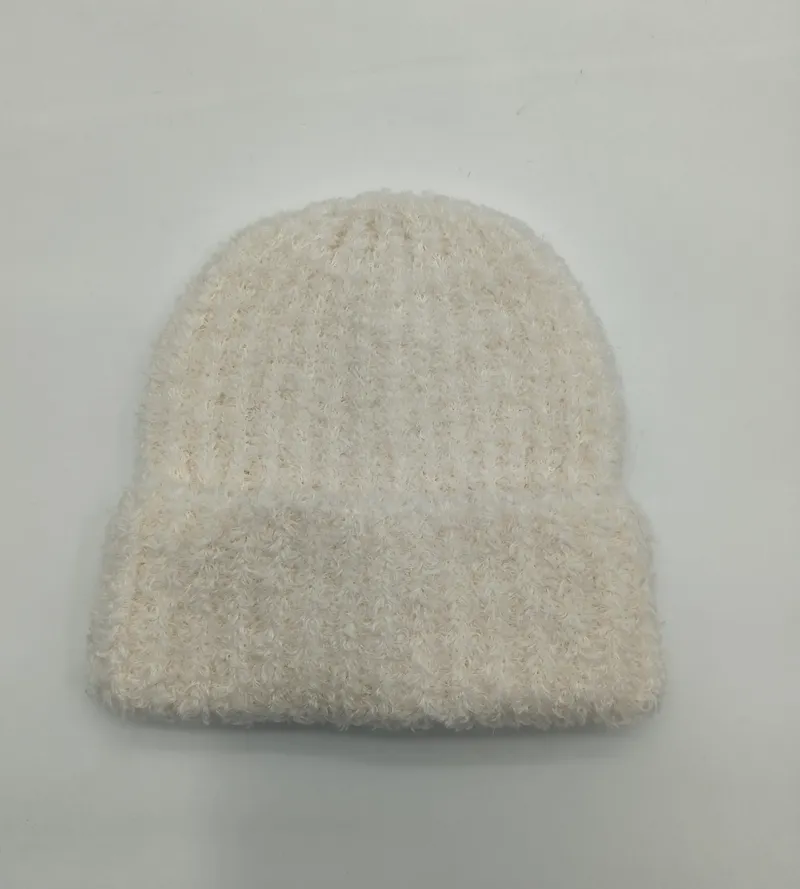 Weiche cremeweiße Wintermütze mit fluffiger Strickstruktur und lockerem Sitz, von oben fotografiert auf hellem Untergrund