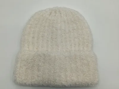 Weiche cremeweiße Wintermütze mit fluffiger Strickstruktur und lockerem Sitz, von oben fotografiert auf hellem Untergrund