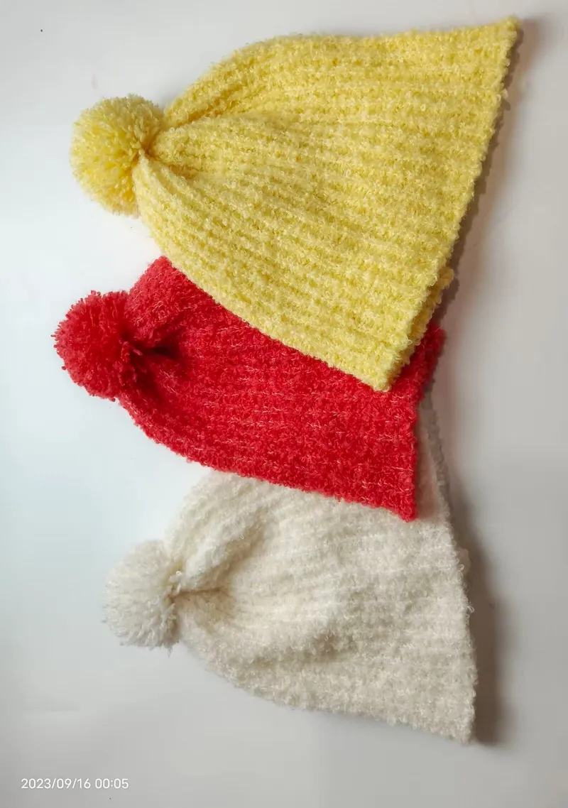 Drei flauschige Chenille-Strickmützen mit Bommel in Gelb, Rot und Weiß übereinandergestapelt vor weißem Hintergrund