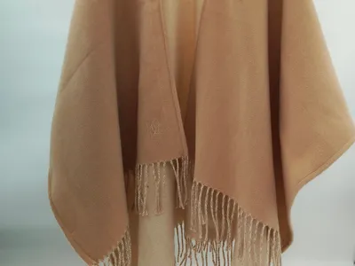 Eleganter Wickelponcho in Sandbeige aus weichem Wollgemisch mit langen Fransensäumen und offenem Schnitt, auf Kleiderbügel präsentiert