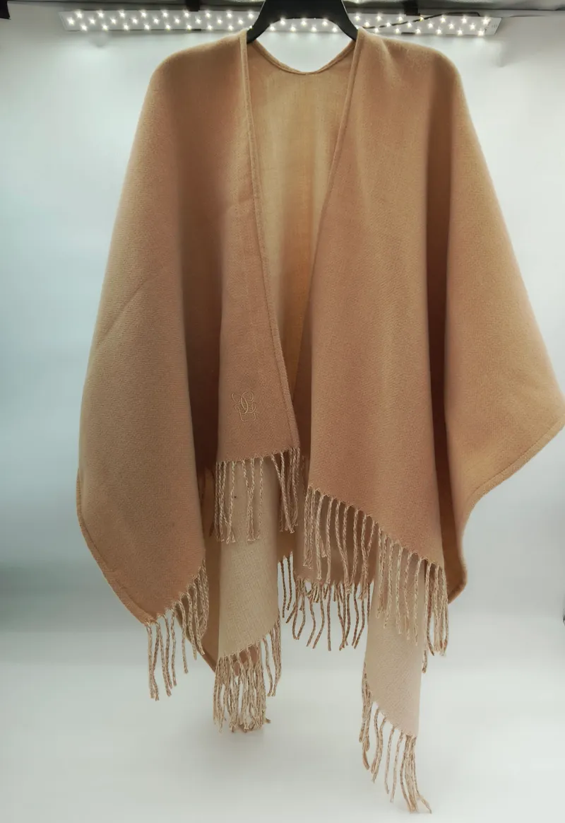 Eleganter Wickelponcho in Sandbeige aus weichem Wollgemisch mit langen Fransensäumen und offenem Schnitt, auf Kleiderbügel präsentiert